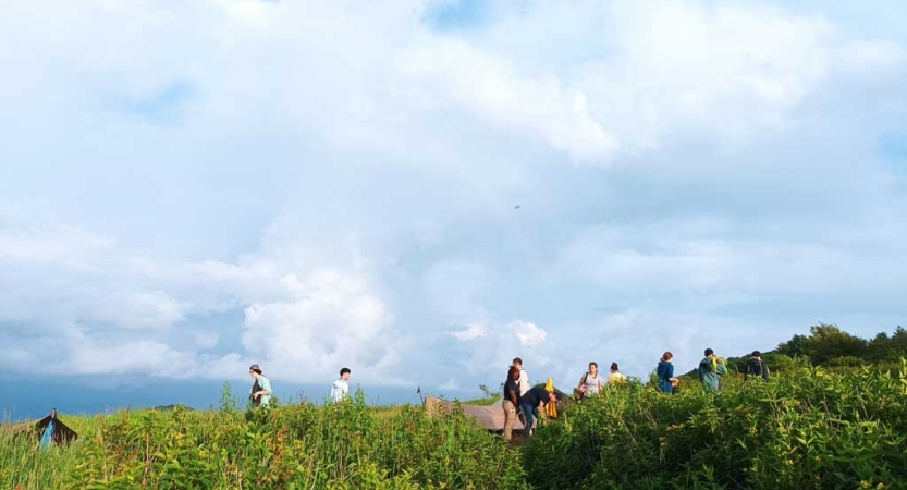 A group of students make camp with tarp shelters under a cloudy sky